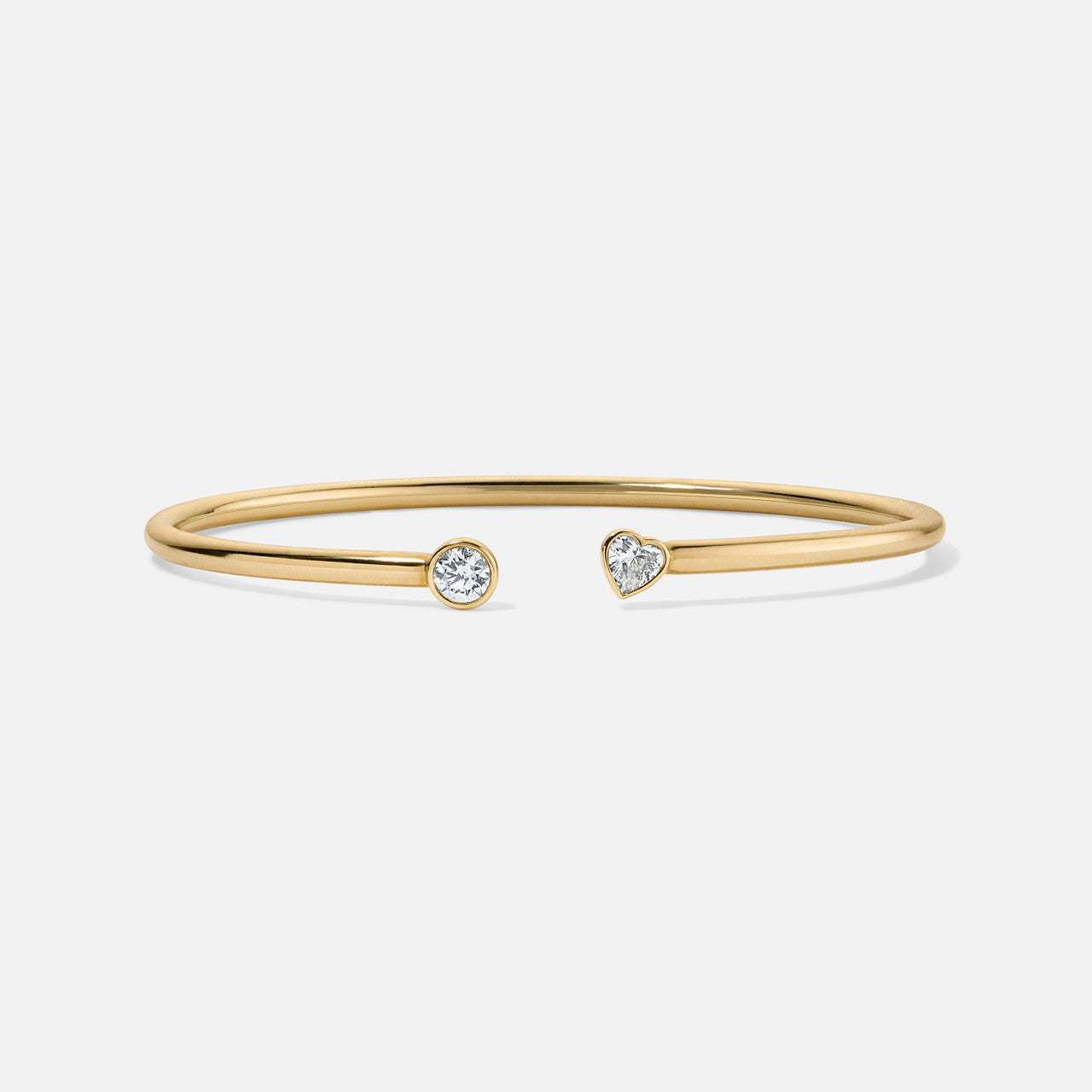an open cuff bracelet that has a heart shaped diamond on the right side and a round diamond on the left