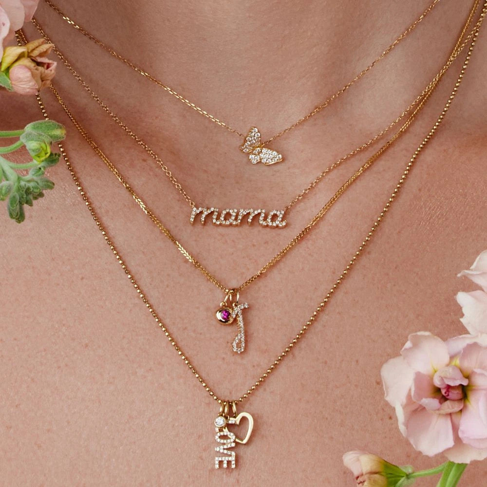 A gold pendant featuring a diamond-studded initial, among layers of necklaces.