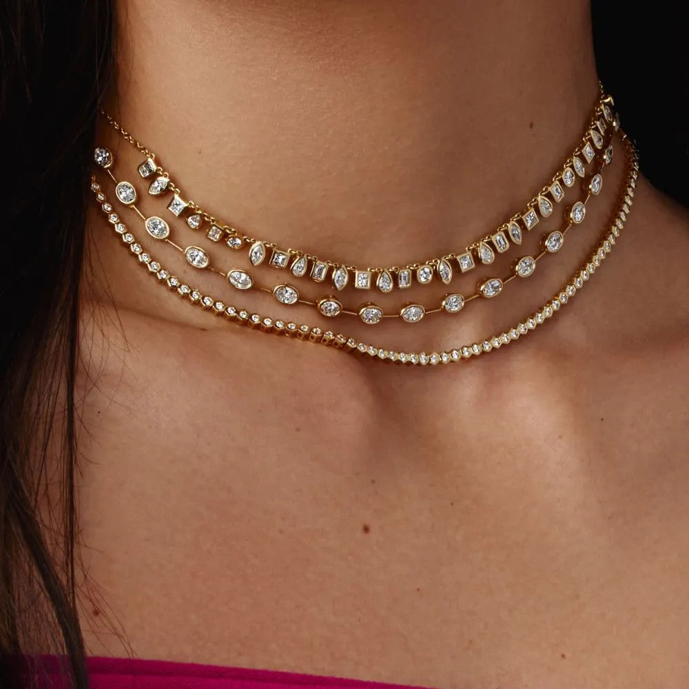 A woman wears three necklaces. The middle necklace is a Razny Exclusive yellow gold necklace features 40 bezel-set oval diamonds in a sleek bar-style design.